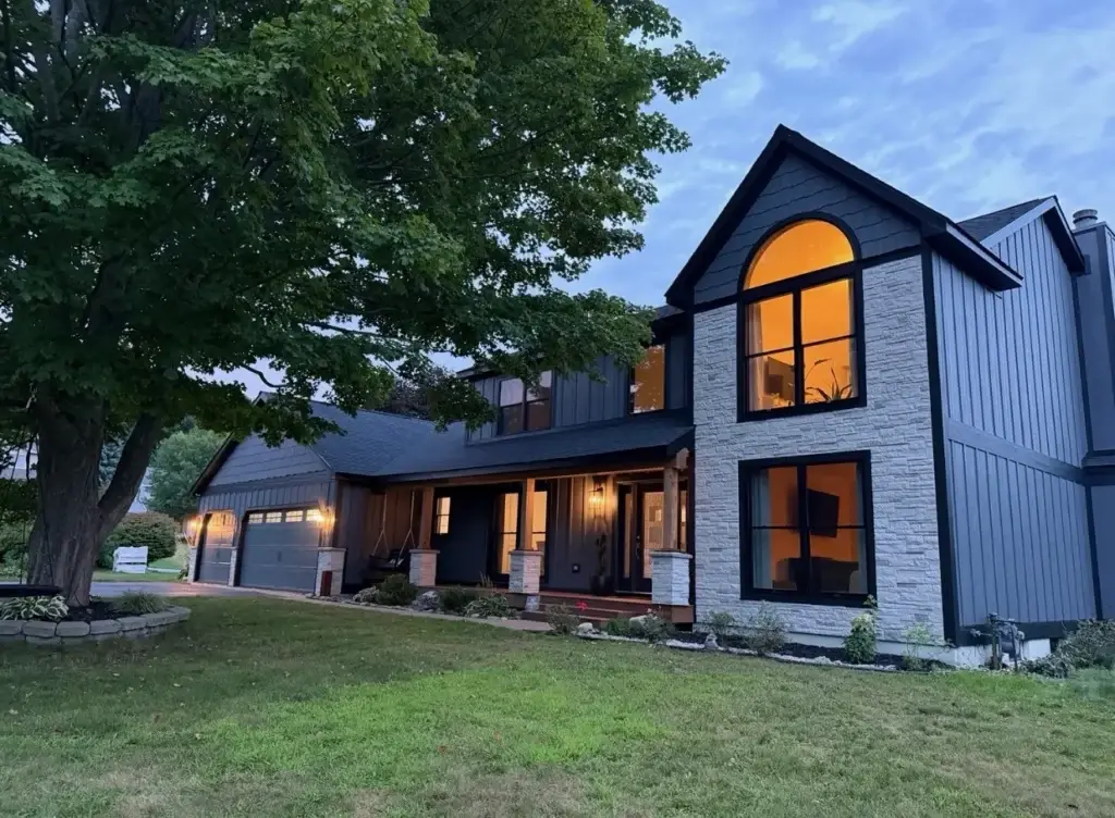After: black board-and-batten exterior with white stone and glowing windows at dusk