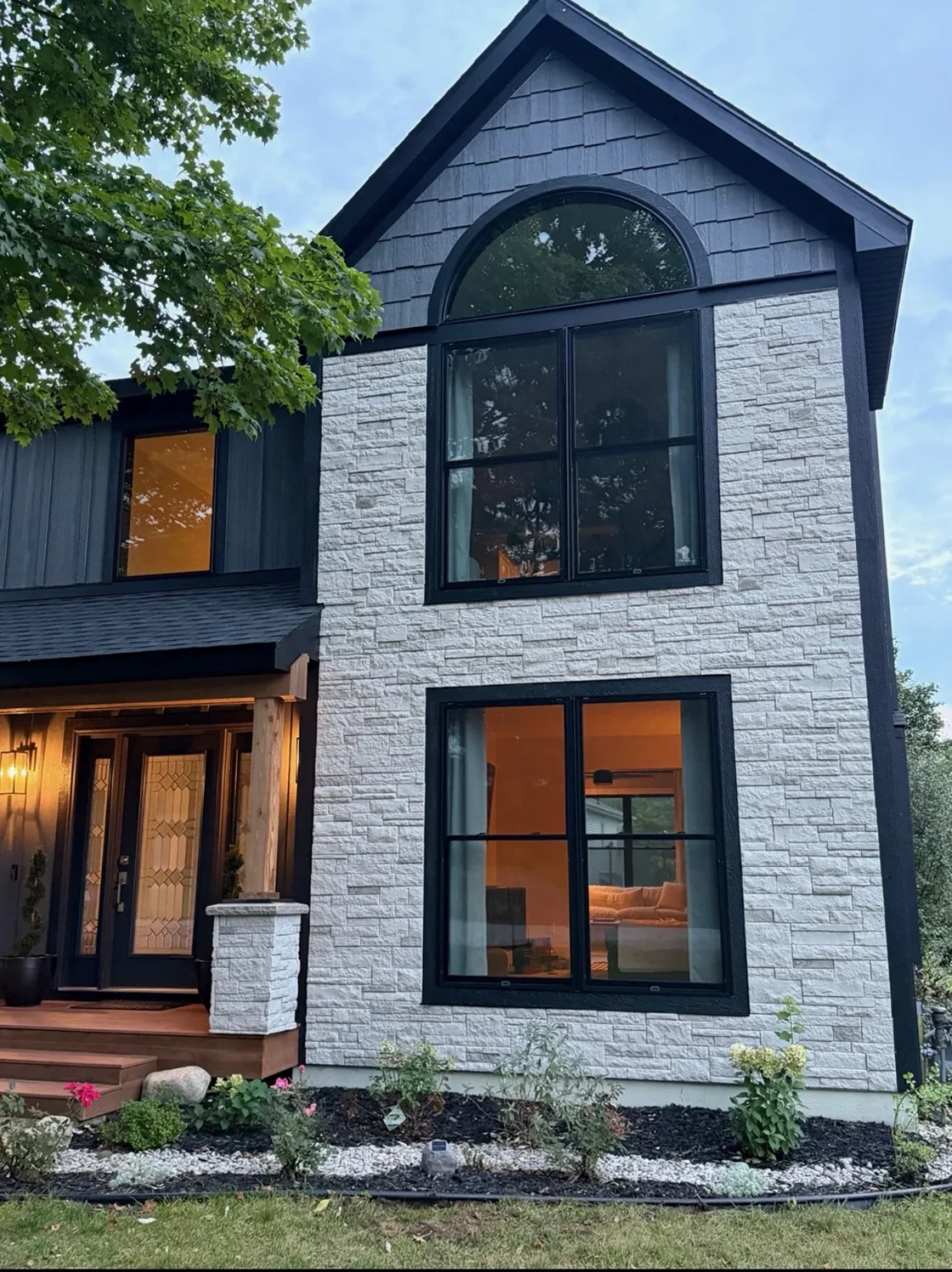 After: white stacked-stone gable with black-framed arched window at dusk