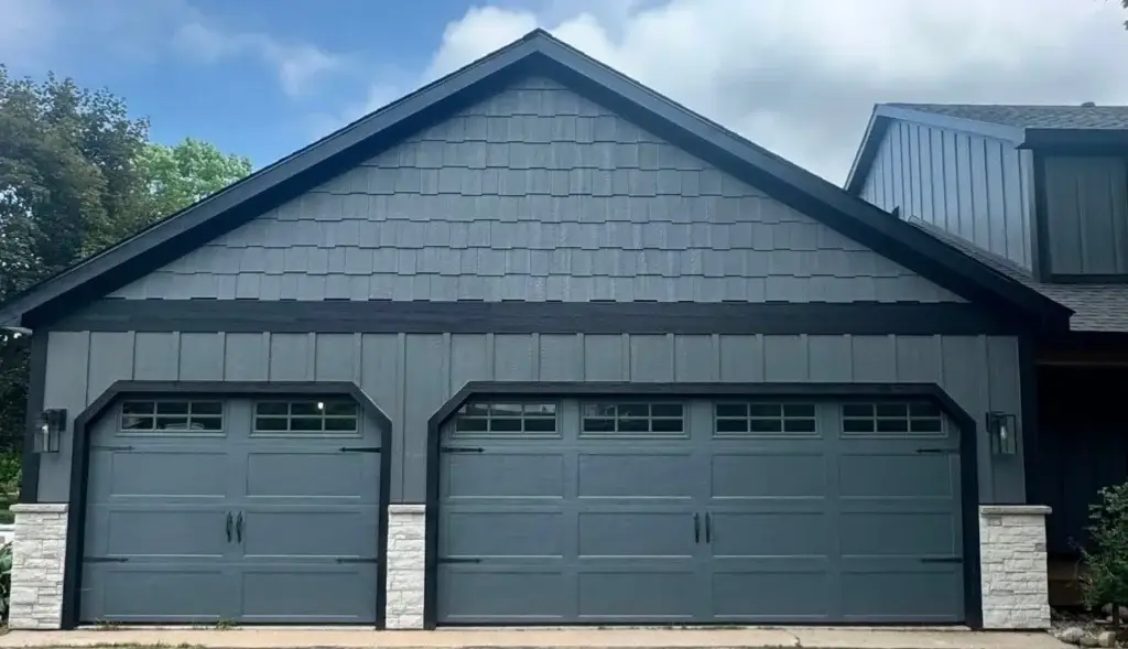 After: charcoal carriage-style garage doors with shake gable and stone piers