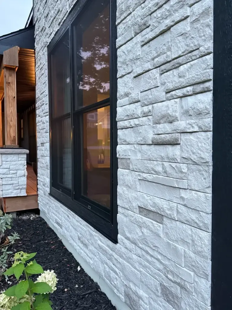 After: white stacked-stone wall and black window frame detail at dusk