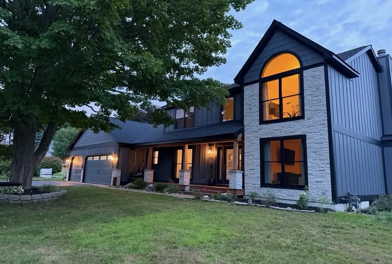 After at dusk: charcoal board-and-batten, white stone and glowing black-framed windows